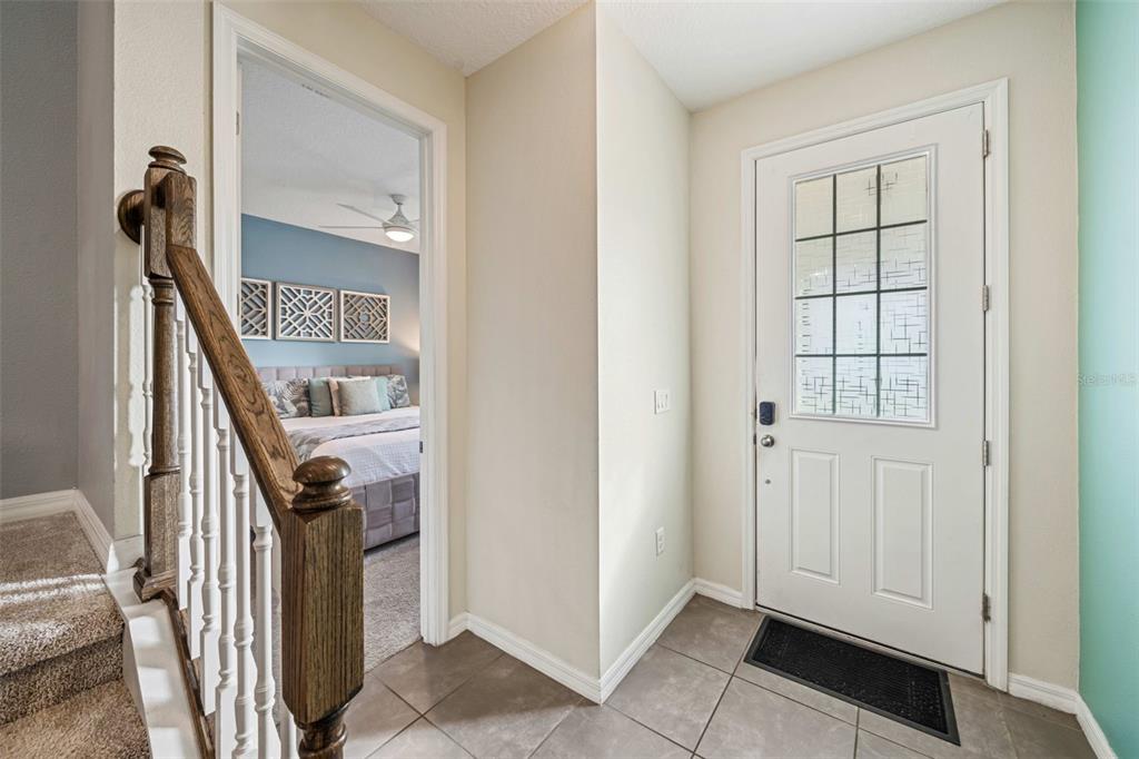 An entryway with tiled flooring, a wooden staircase, and a doorway leading to a bedroom — 9079 SUNSHINE RIDGE LOOP, KISSIMMEE, FL