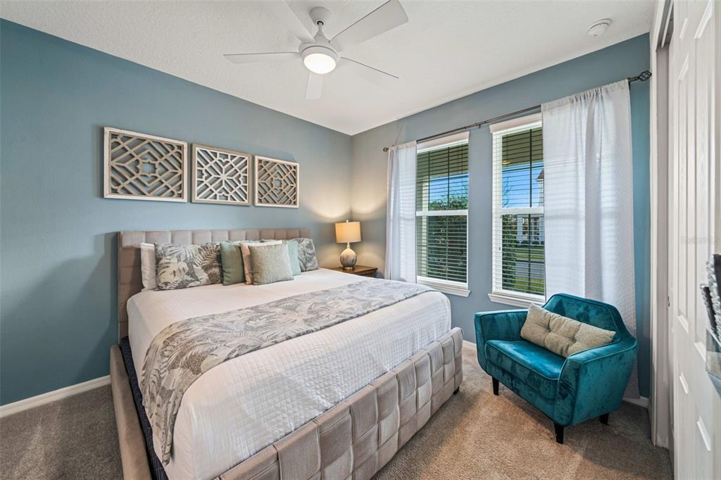 A bedroom features a tufted bed, a teal armchair, and blue walls with decorative panels — 9079 SUNSHINE RIDGE LOOP, KISSIMMEE, FL