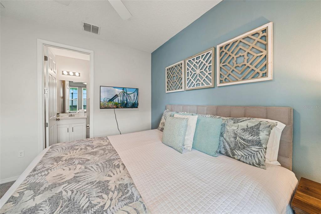 A bedroom features a bed with patterned bedding, a blue accent wall, and wall art — 9079 SUNSHINE RIDGE LOOP, KISSIMMEE, FL
