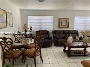 A living and dining room area with tile floors, brown furniture, and two windows — 1300 W 53rd St # 19, Hialeah FL 33012, HIALEAH, FL