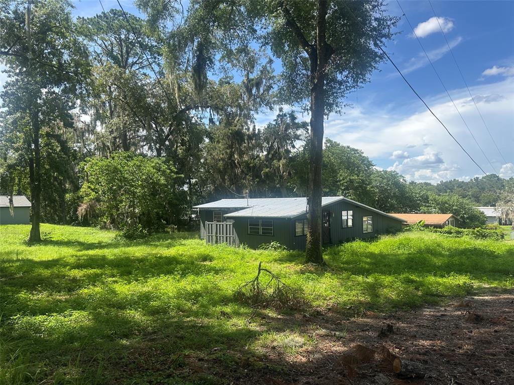 A gray house with a metal roof sits on a grassy lot surrounded by trees — 1610 NE 14TH AVENUE, OCALA, FL