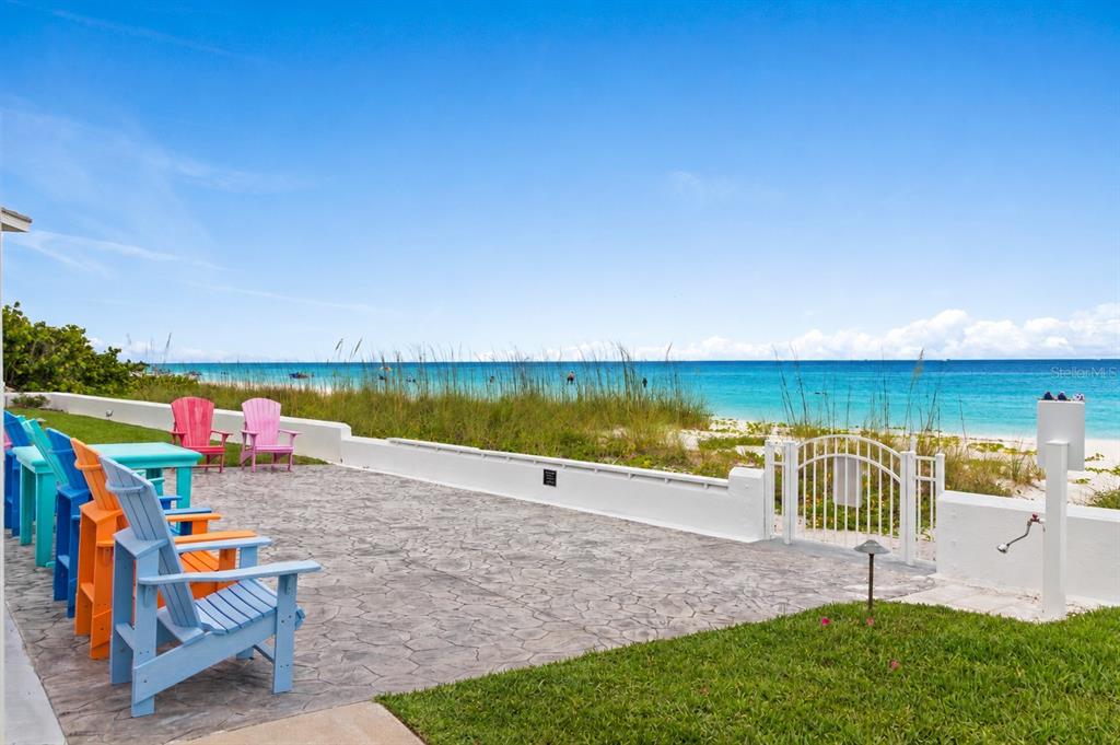 A patio with colorful Adirondack chairs overlooks a sandy beach and the ocean — 5400 GULF DRIVE UNIT 18, HOLMES BEACH, FL