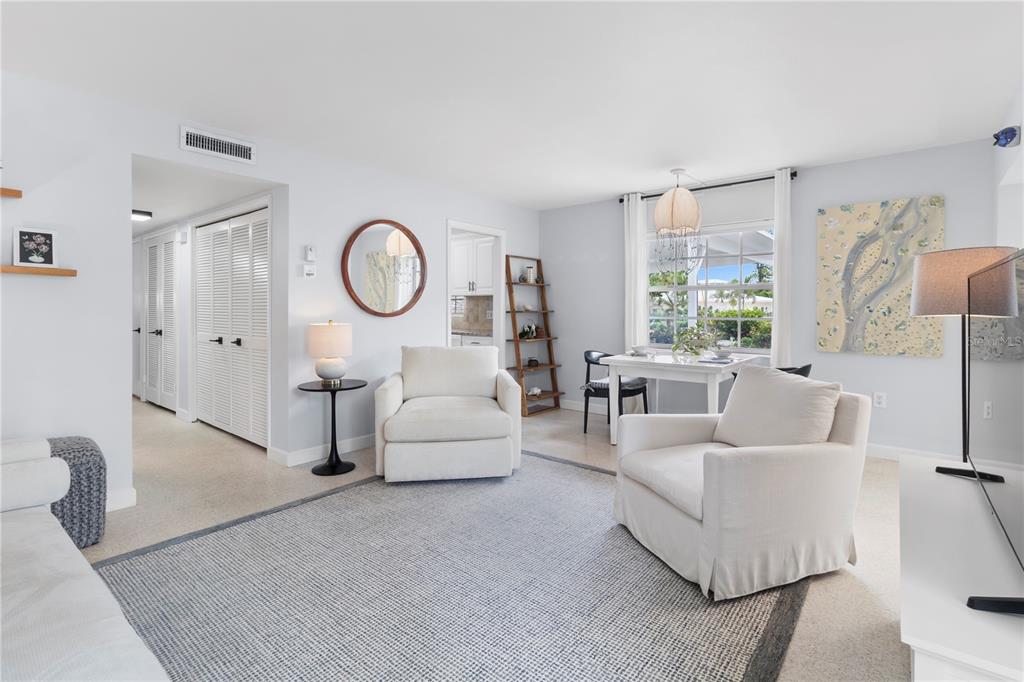 A bright living room features two white armchairs, a dining area, and a large rug — 5400 GULF DRIVE UNIT 18, HOLMES BEACH, FL