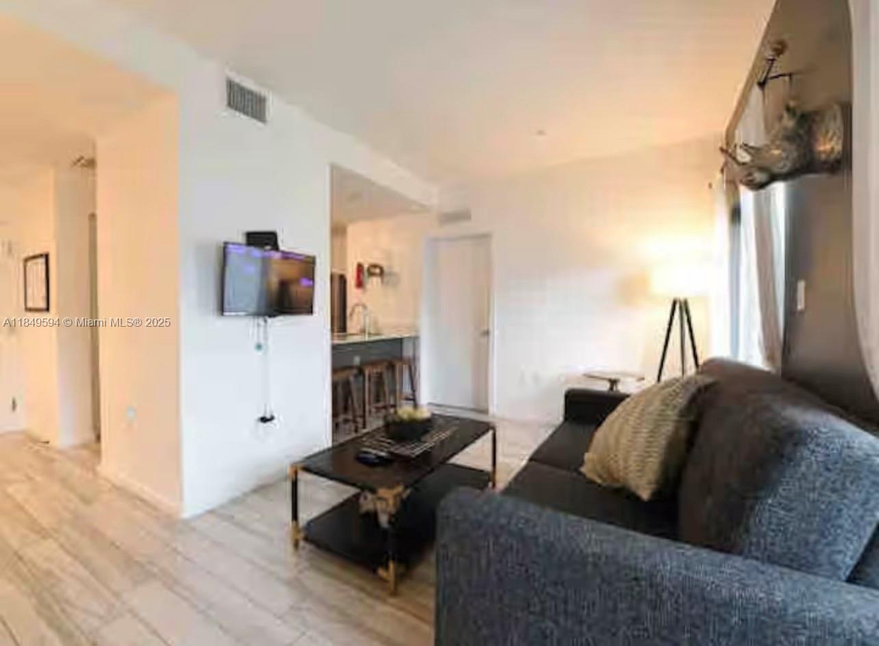 A living room features a dark sofa, a coffee table, and a wall-mounted television — 481 NE 29th St # 705, Miami FL 33137, MIAMI, FL