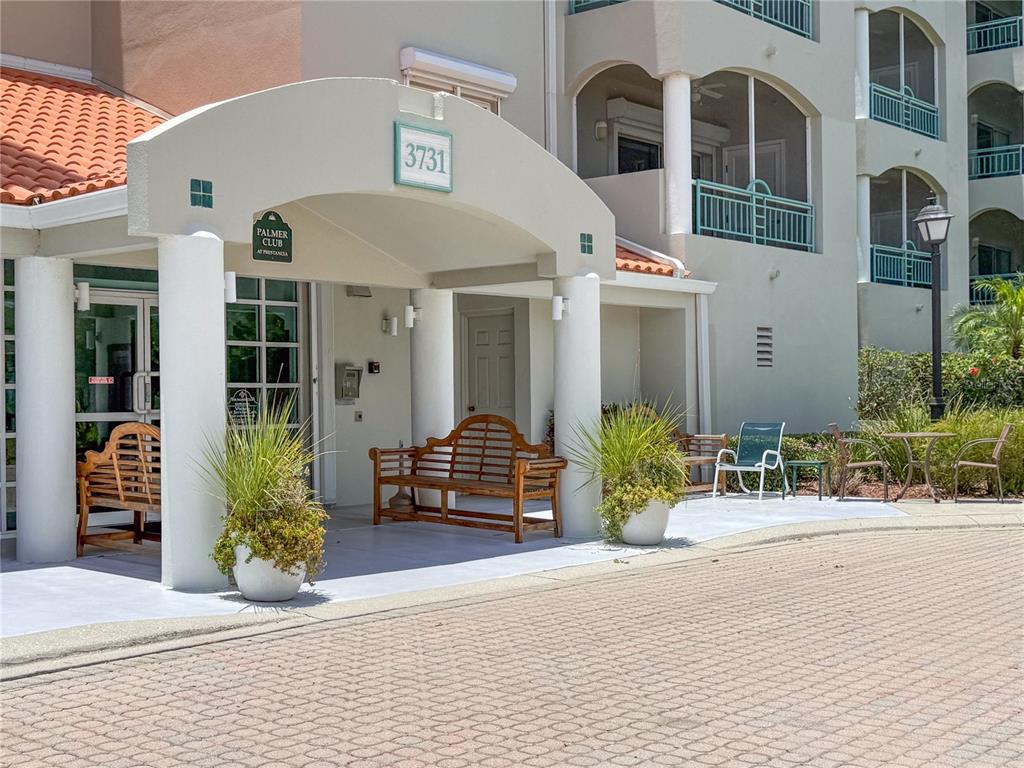 The exterior entrance of a building features a covered walkway with benches and potted plants — 3731 SARASOTA SQUARE BOULEVARD UNIT 309E, SARASOTA, FL