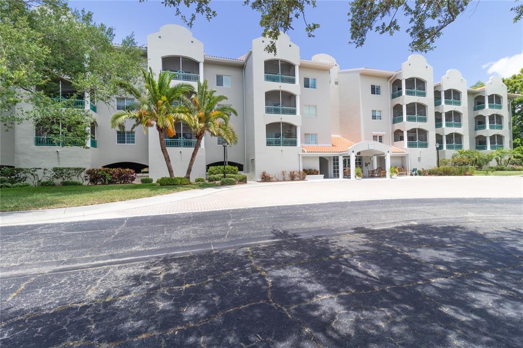 A multi-story apartment building with arched balconies and a covered entrance sits behind a driveway — 3731 SARASOTA SQUARE BOULEVARD UNIT 309E, SARASOTA, FL