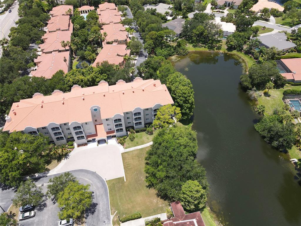 An aerial view shows a multi-story apartment building with a tiled roof beside a pond — 3731 SARASOTA SQUARE BOULEVARD UNIT 309E, SARASOTA, FL
