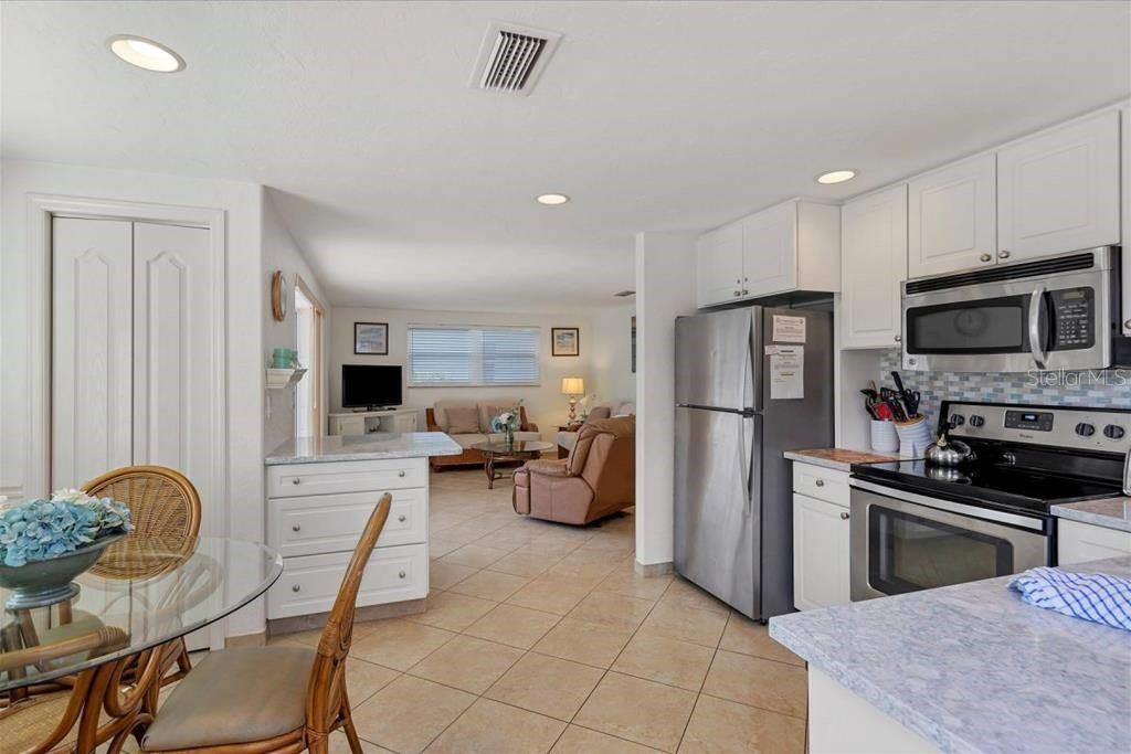 A kitchen with white cabinets and stainless steel appliances opens to a living room area — 6154 MIDNIGHT PASS ROAD UNIT C12, SARASOTA, FL