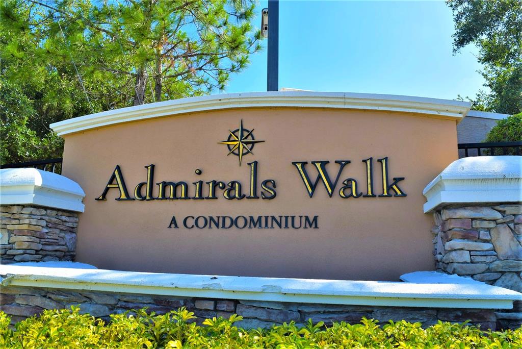 A tan monument sign for Admirals Walk A Condominium stands outdoors with stone pillars — 5711 SOLDIER CIRCLE UNIT # 102, SARASOTA, FL