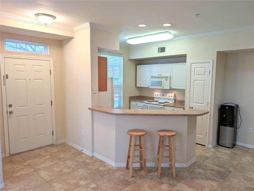 A kitchen with white cabinets, a breakfast bar with two stools, and tile flooring — 5711 SOLDIER CIRCLE UNIT # 102, SARASOTA, FL
