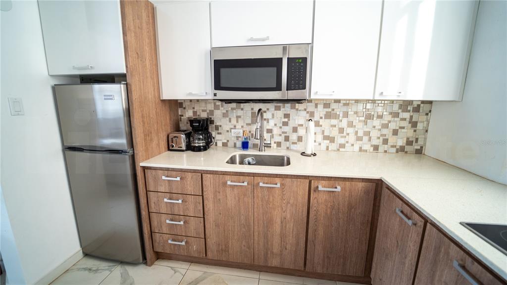 A kitchen features wood-grain lower cabinets, white upper cabinets, stainless steel appliances, and tiled backsplash — 101 SOL STREET UNIT 2B, OLD SAN JUAN, PR