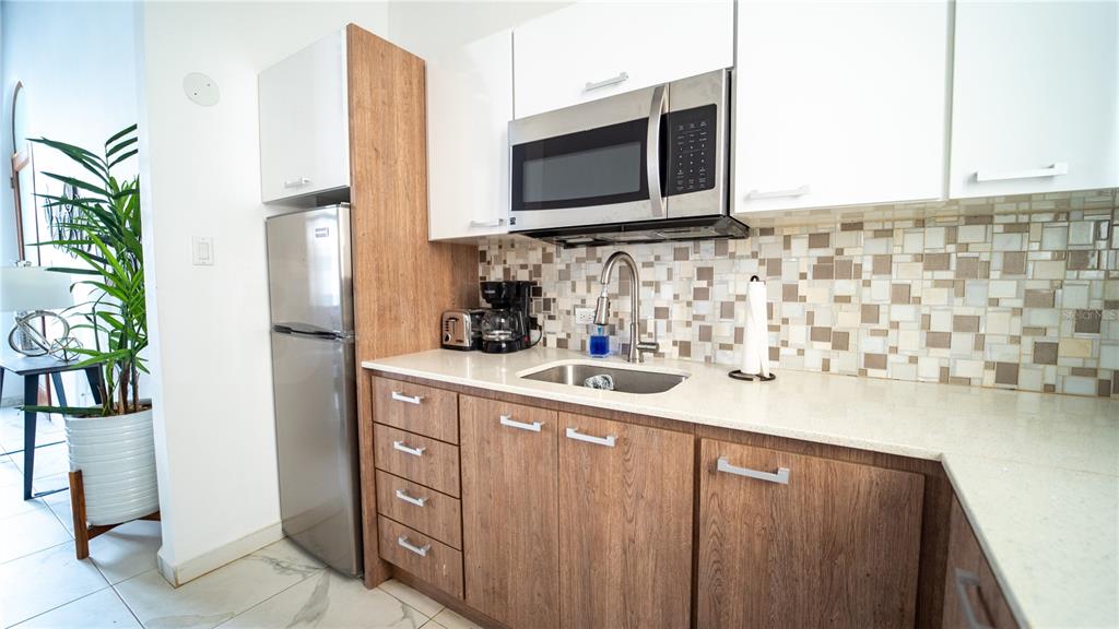 A kitchen features wood-grain lower cabinets, white upper cabinets, a stainless steel microwave, and backsplash — 101 SOL STREET UNIT 2B, OLD SAN JUAN, PR