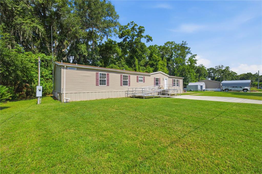 A tan manufactured home with a metal wheelchair ramp sits on a large grassy lawn — 8450 NW 15TH AVENUE, OCALA, FL