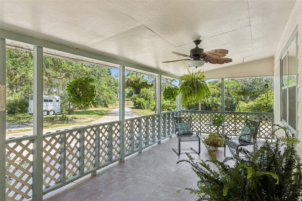 A covered porch features a ceiling fan, lattice railings, hanging plants, and outdoor seating — 8681 DEER RUN DRIVE, LAKE WALES, FL