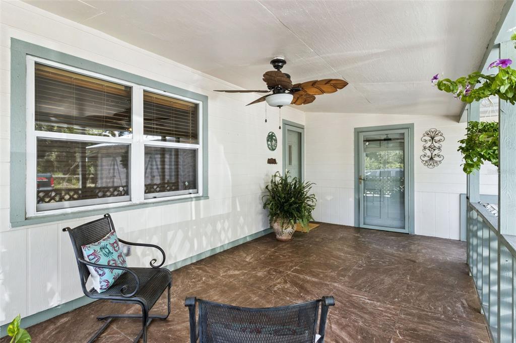 A covered porch features a ceiling fan, tiled floor, two chairs, and a glass door — 8681 DEER RUN DRIVE, LAKE WALES, FL