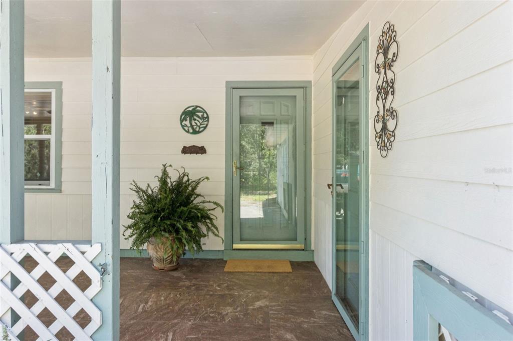 A covered porch features a green screen door, a potted fern, and white siding — 8681 DEER RUN DRIVE, LAKE WALES, FL