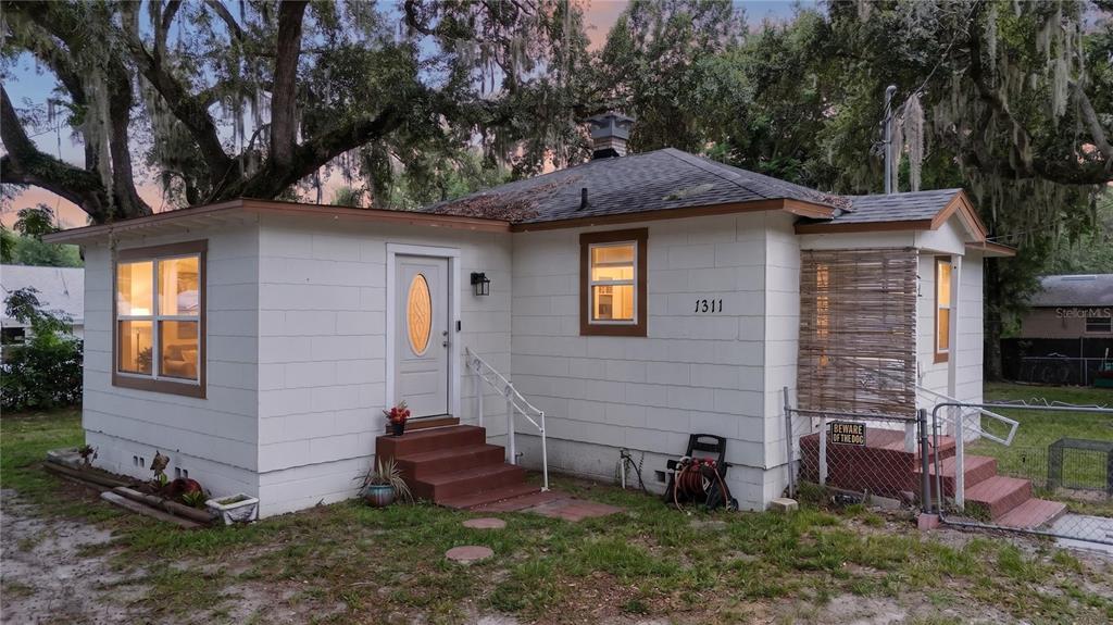 A single-story white house with a brown roof, front steps, and a fenced side porch — 1311 SUMTER STREET, LEESBURG, FL