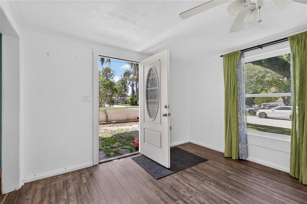 An interior view of a room with wood-look flooring, white walls, and an open front door — 1311 SUMTER STREET, LEESBURG, FL