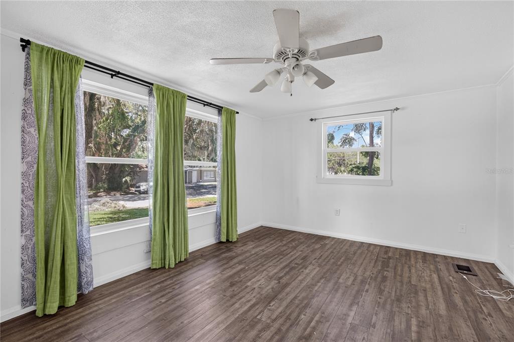 An empty bedroom features white walls, dark wood-look flooring, a ceiling fan, and green curtains — 1311 SUMTER STREET, LEESBURG, FL