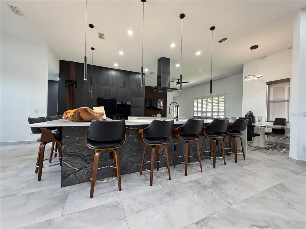 A modern kitchen features a large marble-topped island with five black stools and dark cabinetry — 4419 SADDLEWORTH CIRCLE, ORLANDO, FL