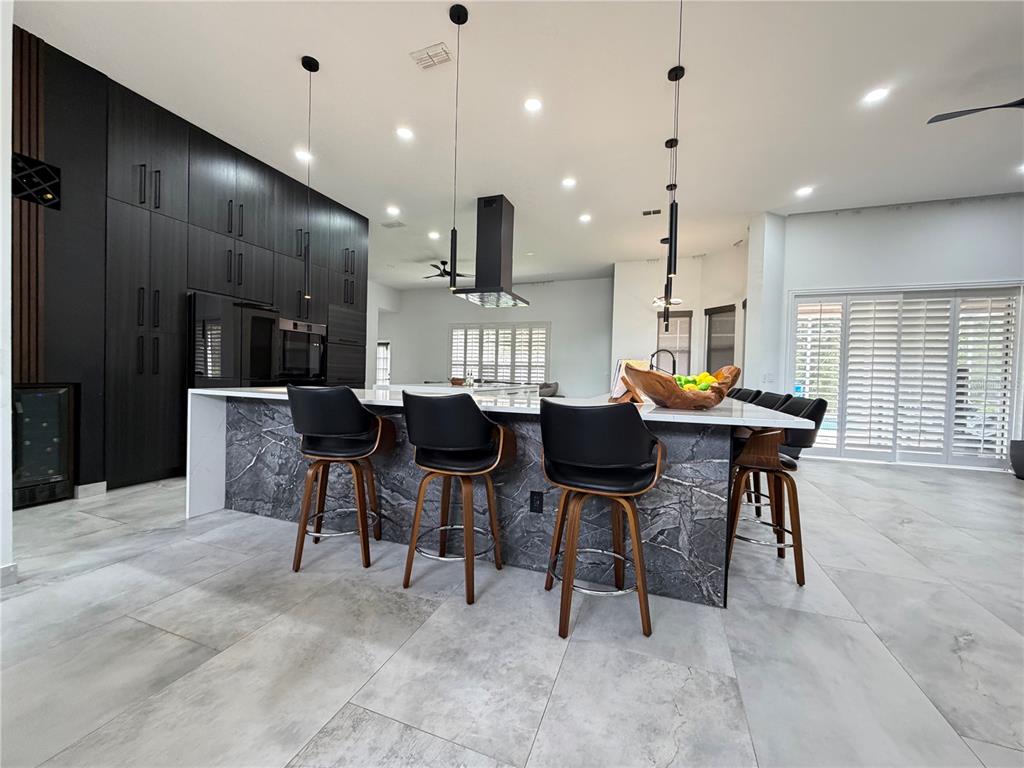 A modern kitchen features a large marble-topped island with bar stools and dark cabinetry — 4419 SADDLEWORTH CIRCLE, ORLANDO, FL