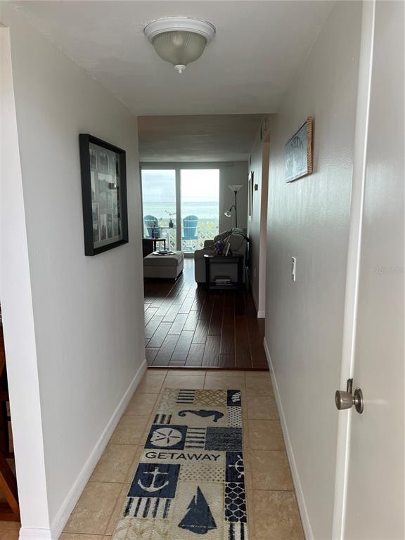A hallway with tile flooring leads to a living area with wood floors and ocean views — 9 FORBES PLACE UNIT 405, DUNEDIN, FL