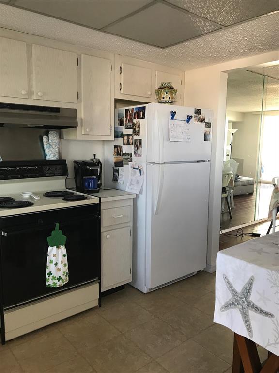 A kitchen features white cabinets, a black stove, a white refrigerator, and tiled flooring — 9 FORBES PLACE UNIT 405, DUNEDIN, FL