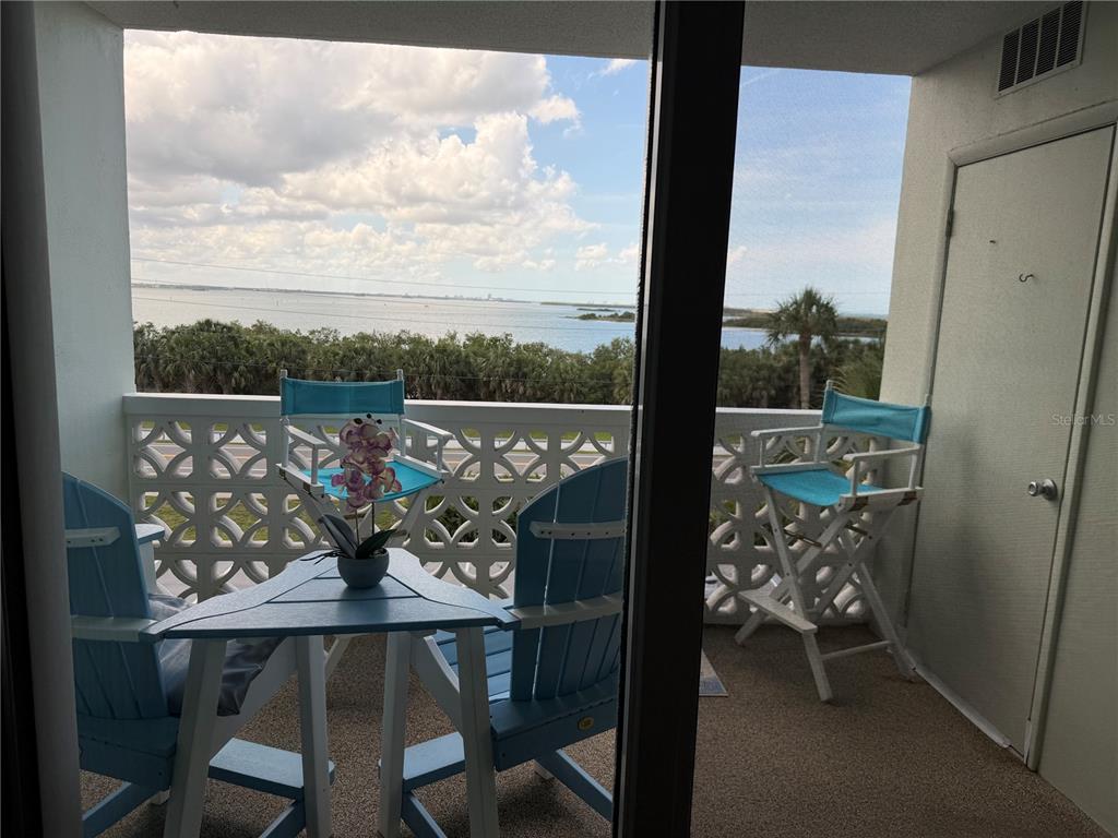 A balcony with blue patio furniture overlooks a body of water and trees — 9 FORBES PLACE UNIT 405, DUNEDIN, FL