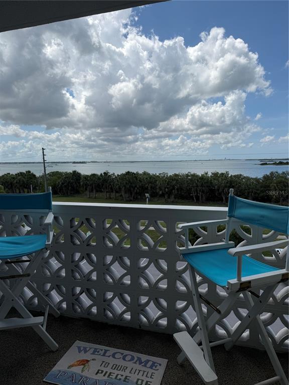 A balcony with two blue director chairs overlooks a body of water and palm trees — 9 FORBES PLACE UNIT 405, DUNEDIN, FL