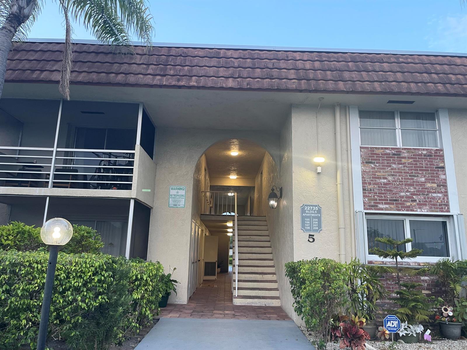 The exterior of a two-story apartment building features a central arched entryway with stairs — 22735 SW 66th Avenue, Boca Raton FL 33428, BOCA RATON, FL