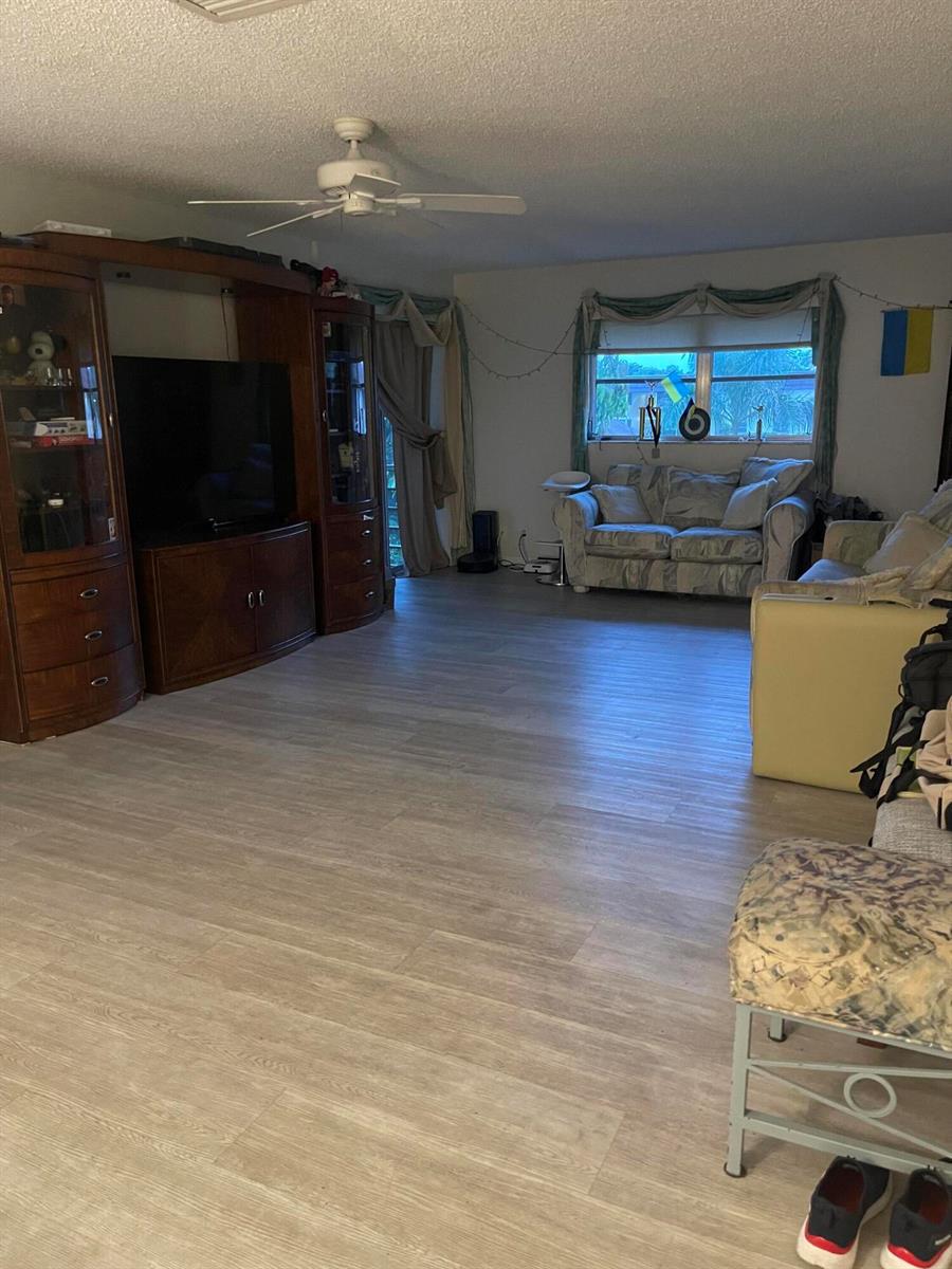 A living room features light wood-look flooring, a large wooden entertainment center, and two sofas — 22735 SW 66th Avenue, Boca Raton FL 33428, BOCA RATON, FL