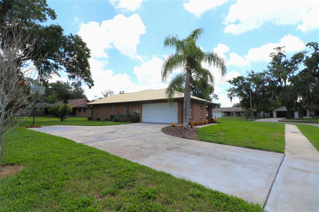 A brick house with a yellow metal roof and a concrete driveway under a palm tree — 1023 REDBUD CIRCLE, PLANT CITY, FL