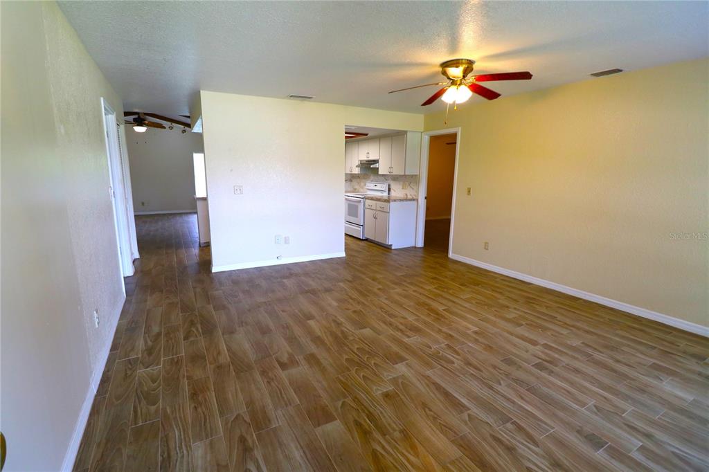 A living room with wood-look tile flooring leads to a kitchen and a hallway — 1023 REDBUD CIRCLE, PLANT CITY, FL