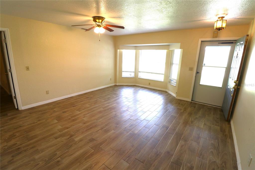 A living room features wood-look tile flooring, a ceiling fan, and a bay window — 1023 REDBUD CIRCLE, PLANT CITY, FL