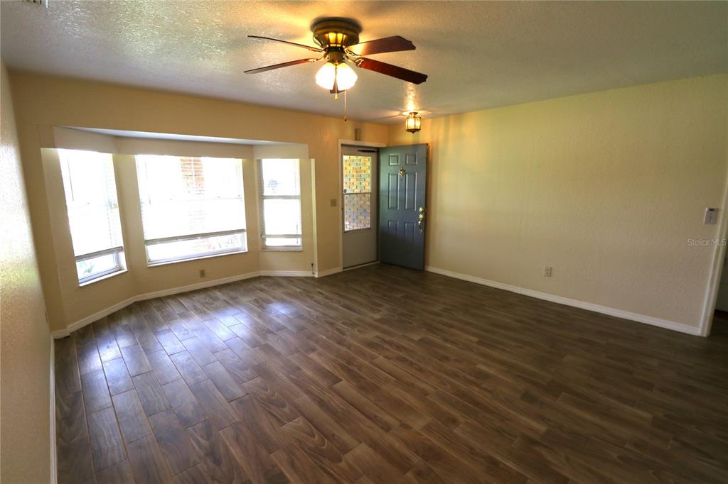 An empty living room features wood-look tile flooring, a ceiling fan, and a bay window — 1023 REDBUD CIRCLE, PLANT CITY, FL