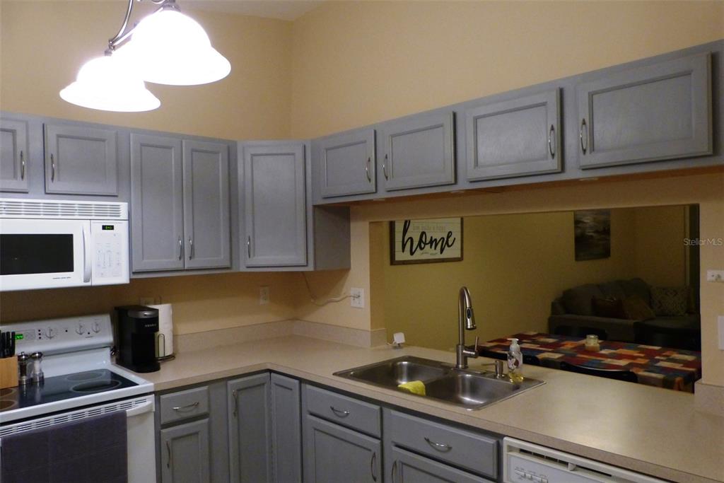 A kitchen features gray cabinets, beige countertops, a double sink, and a white microwave — 1610 SEASCAPE CIRCLE UNIT 1610, TARPON SPRINGS, FL