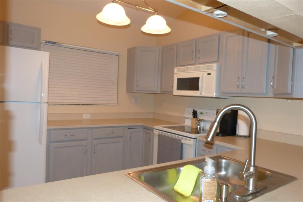 A kitchen features gray cabinets, white appliances, a stainless steel sink, and light countertops — 1610 SEASCAPE CIRCLE UNIT 1610, TARPON SPRINGS, FL