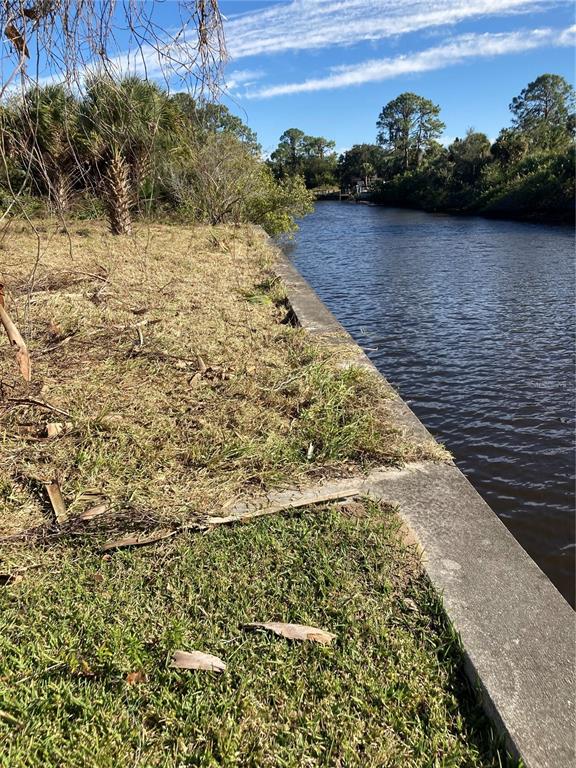 A concrete seawall borders a grassy yard along a narrow canal with trees in background — 12264 CORPORAL CIRCLE, PORT CHARLOTTE, FL