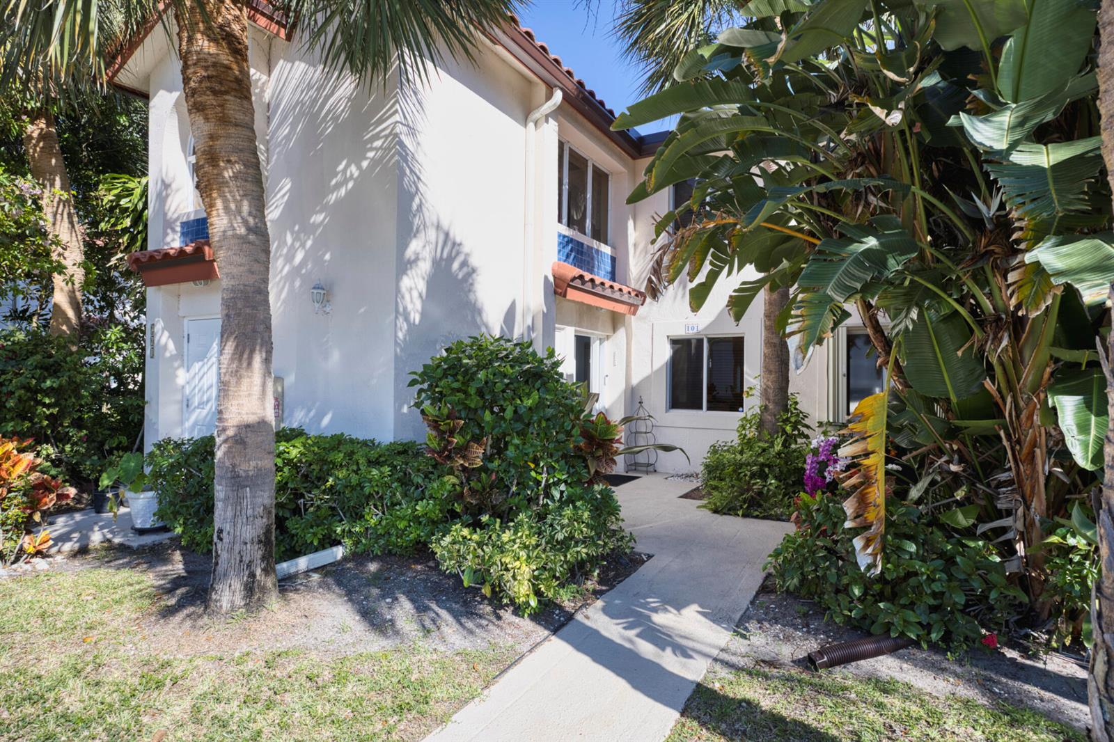 Exterior view of a two-story residential building with a concrete walkway and lush tropical landscaping — 380 NW 67th Street Apt 101, Boca Raton FL 33487, BOCA RATON, FL