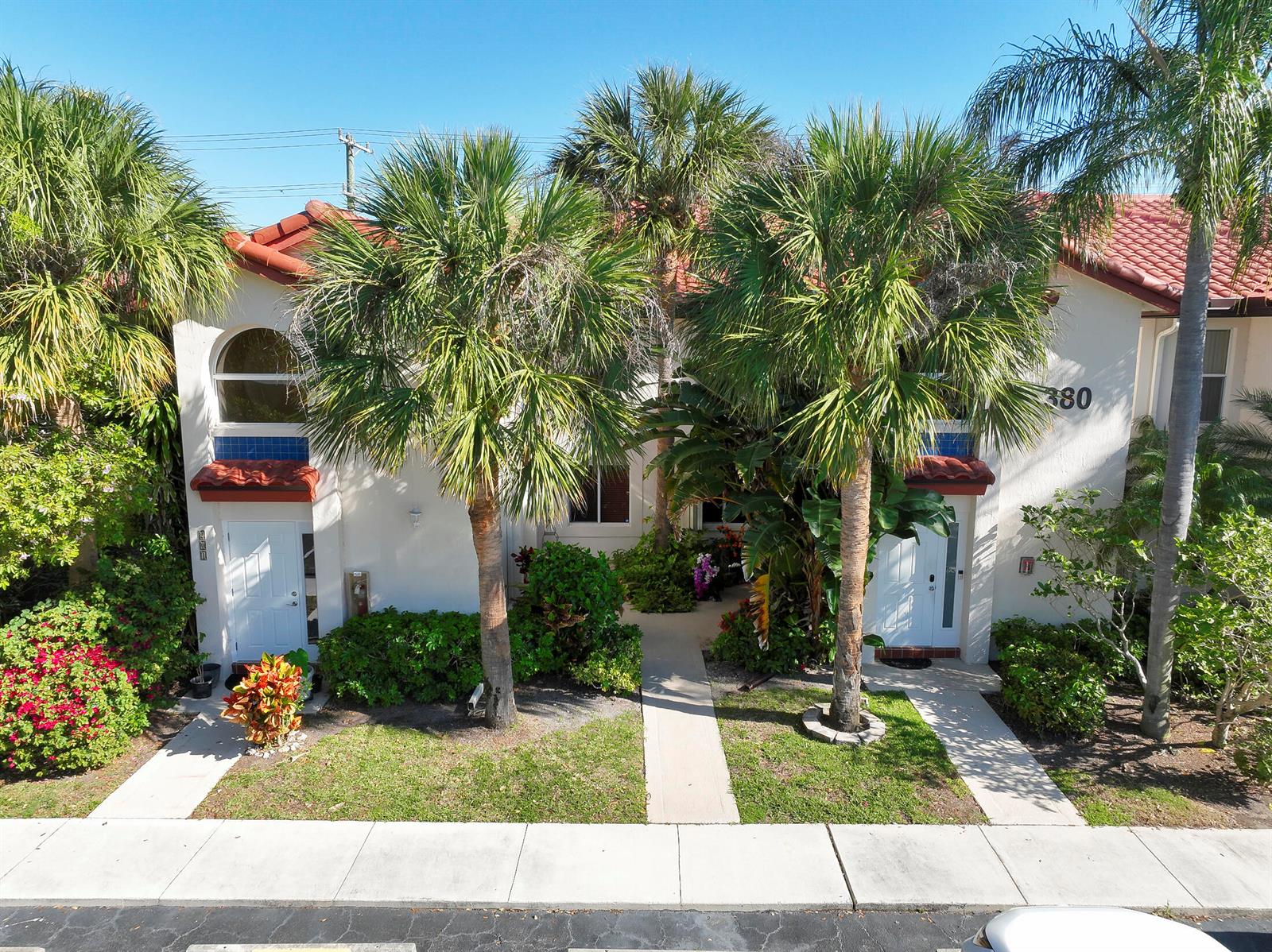 An exterior view of a two-story townhouse with palm trees, a red tile roof, and walkways — 380 NW 67th Street Apt 101, Boca Raton FL 33487, BOCA RATON, FL