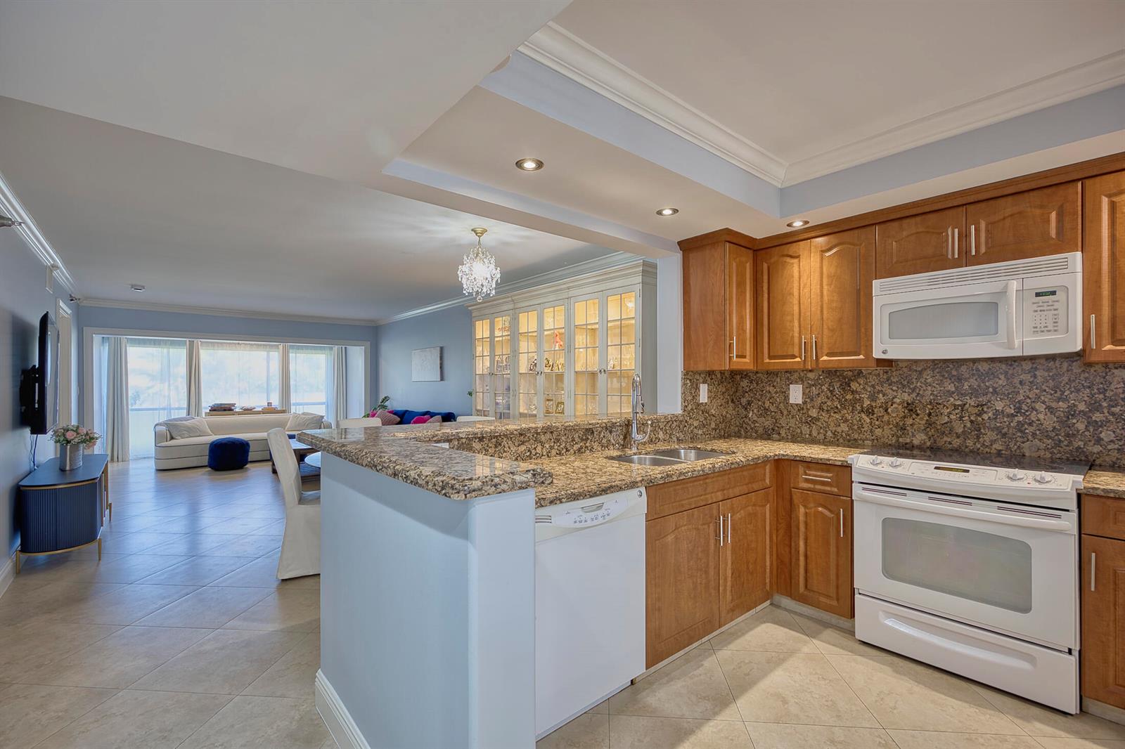 A kitchen with wood cabinets, granite countertops, and white appliances opens to a living area — 380 NW 67th Street Apt 101, Boca Raton FL 33487, BOCA RATON, FL