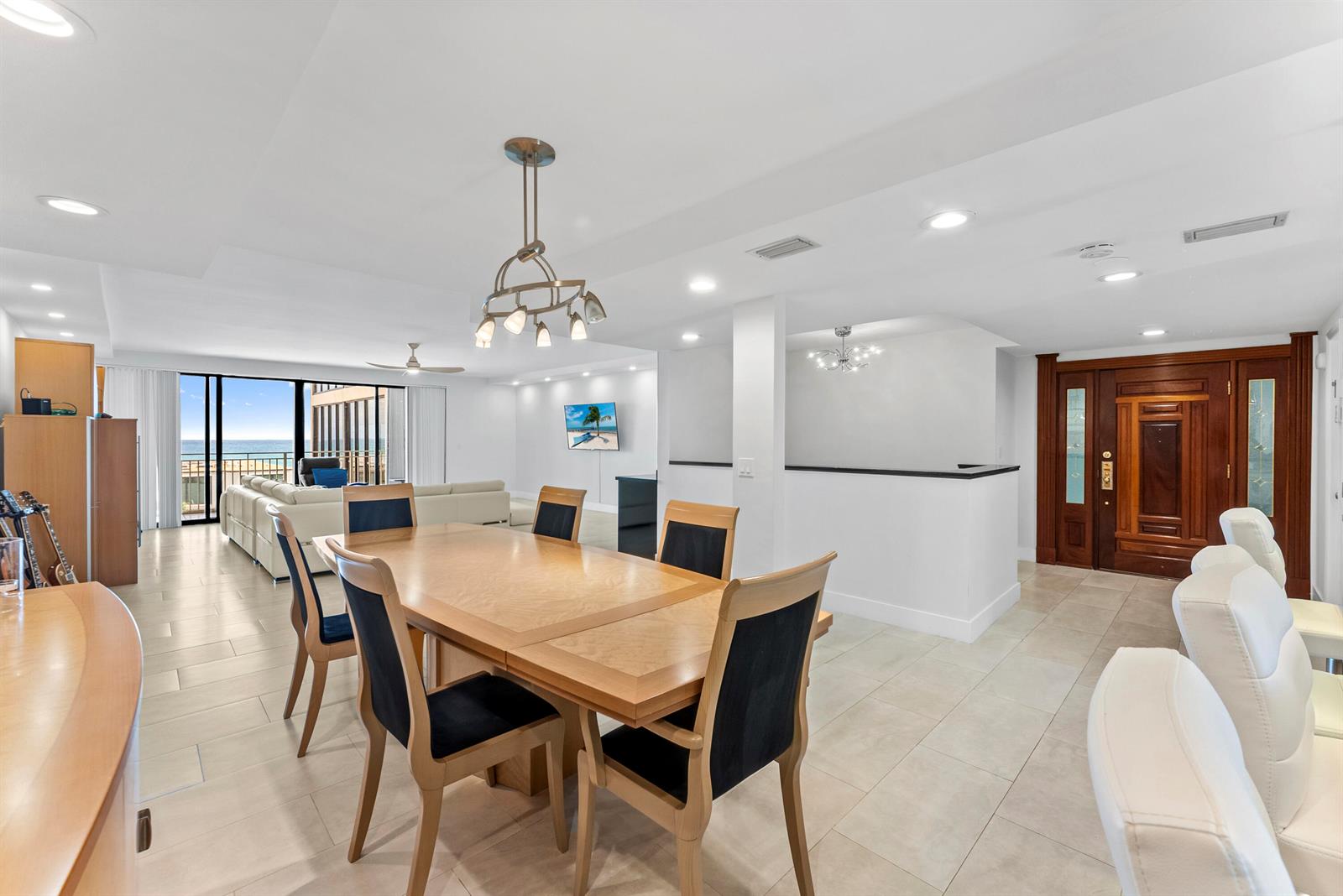A dining area with a wooden table and chairs sits before a bright living room — 2155 S Ocean Boulevard # 11, Delray Beach FL 33483, DELRAY BEACH, FL
