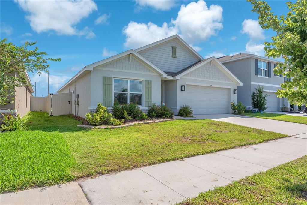 A single-story suburban house with a light gray exterior, a two-car garage, and green shutters — 5166 PLUMERIA DRIVE, WIMAUMA, FL