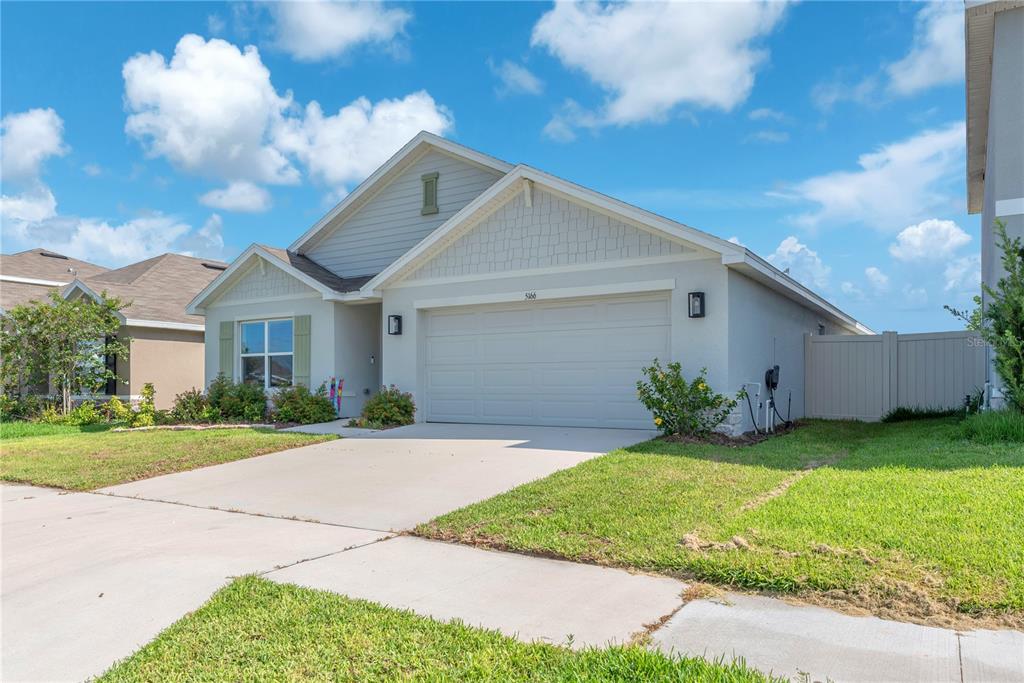 A single-story suburban house with a two-car garage, light siding, and a concrete driveway — 5166 PLUMERIA DRIVE, WIMAUMA, FL