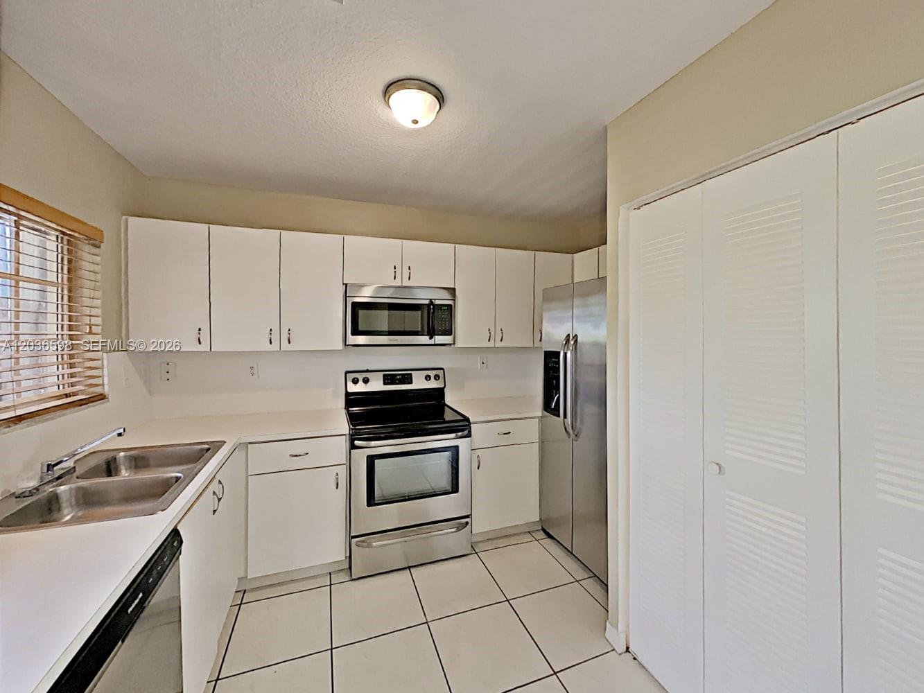 A kitchen features white cabinets, stainless steel appliances, and white tile flooring — MIAMI, FL