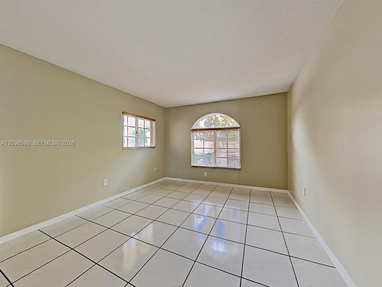 An empty room features beige walls, white tile flooring, and two windows with blinds — MIAMI, FL