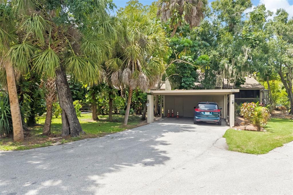 A teal car is parked under a carport in front of a house with palm trees — 5182 LANCEWOOD DRIVE UNIT 14, SARASOTA, FL