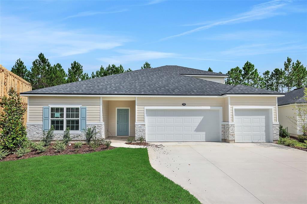A single-story house with light siding, stone accents, a blue front door, and a three-car garage — 3774 HOLSTEIN WAY, GREEN COVE SPRINGS, FL