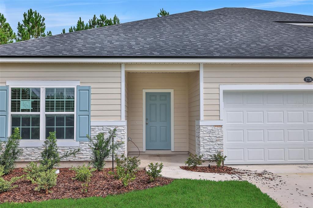 A single-story house exterior features light siding, stone accents, a blue door, and a garage — 3774 HOLSTEIN WAY, GREEN COVE SPRINGS, FL