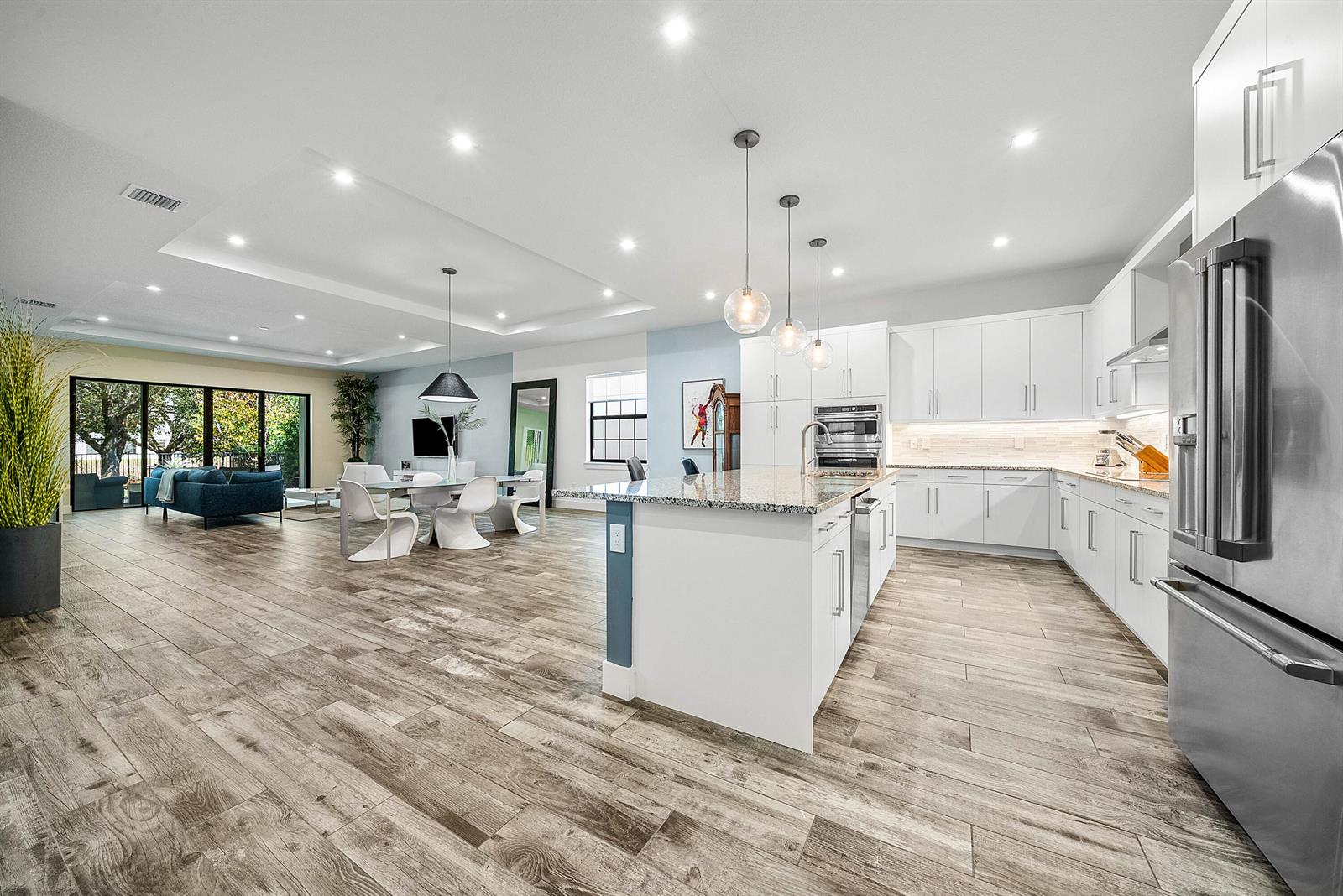A modern open-concept kitchen and living area featuring white cabinetry, granite countertops, and wood-look flooring — 3069 Safflower Circle, West Palm Beach FL 33401, WEST PALM BEACH, FL